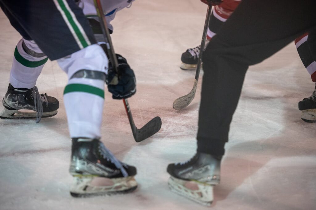 Close-up shot of ice hockey players in an intense face-off, showing skates and sticks on the ice.