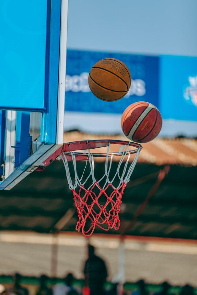 Two basketballs captured mid-air aiming for the hoop on an outdoor court.