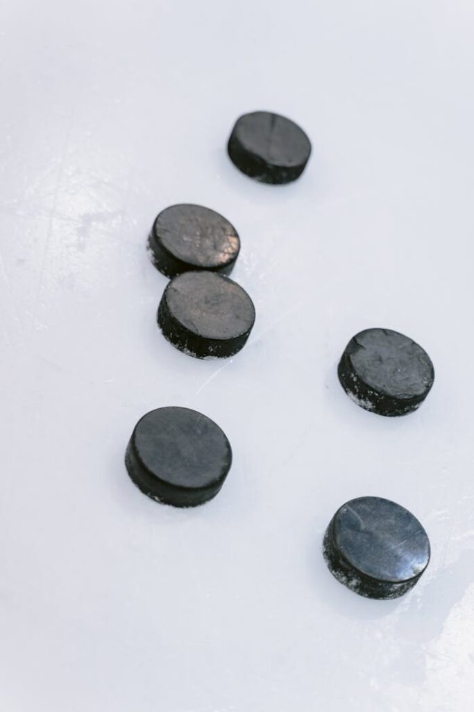Six hockey pucks on an ice rink surface, showcasing sports equipment basics.