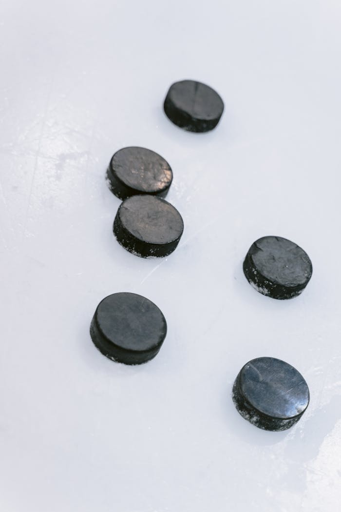 Six hockey pucks on an ice rink surface, showcasing sports equipment basics.